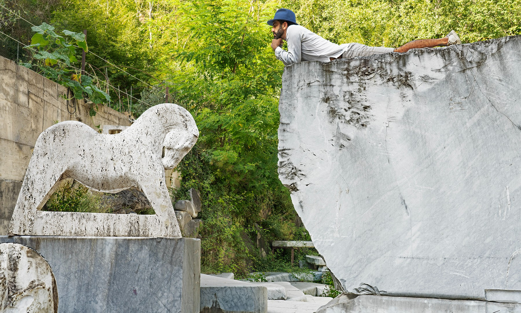 man laying on large marble rock overlooking a stone sculpture of a horse