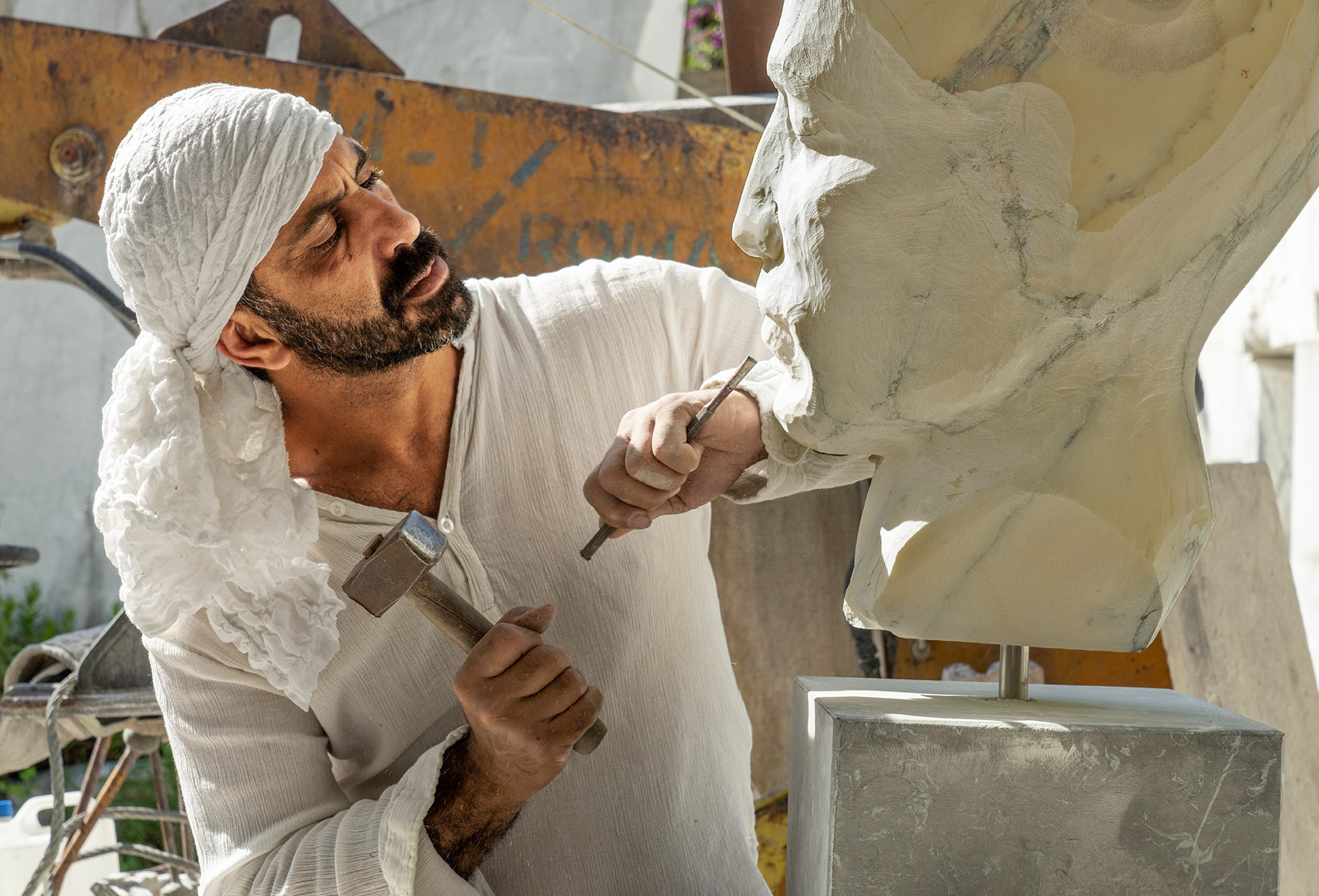 man wearing headscarf carving oversized head in marble