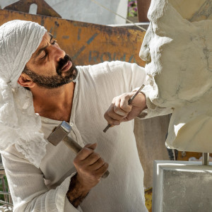 man wearing headscarf carving oversized head in marble