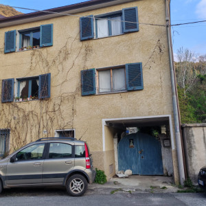 Three story, light terracotta house with blue shutters and vines draped across it.