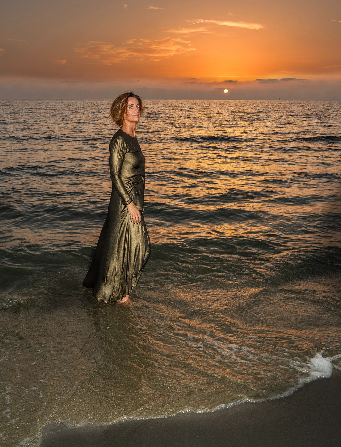 woman standing in ocean surf at sunset