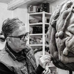 black and white photo os man in glasses working on a sculpture.
