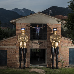 Red brick building with two large gold and black statues of men and human man stood on the balcony.