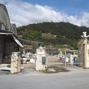 Large building with metal gates leading to marble workshop against a backdrop of green hills.