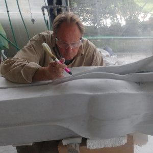 man with dremel tool working on a white marble sculpture.