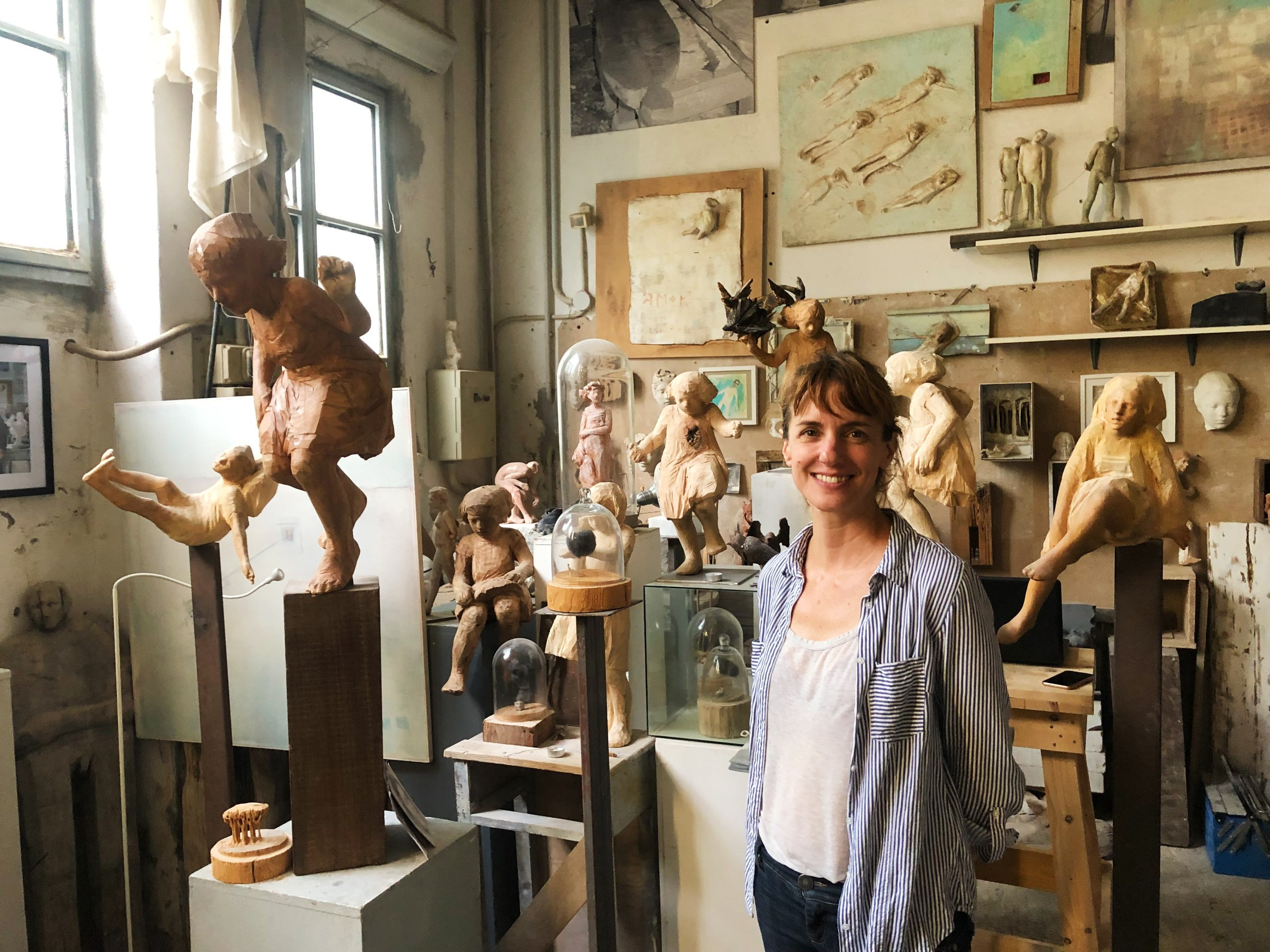 smiling female artist standing in studio full of sculptures