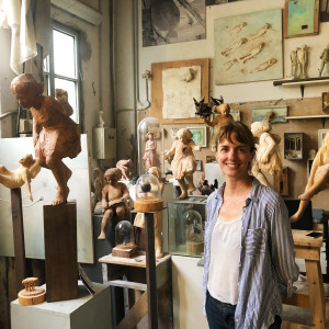 smiling female artist standing in studio full of sculptures