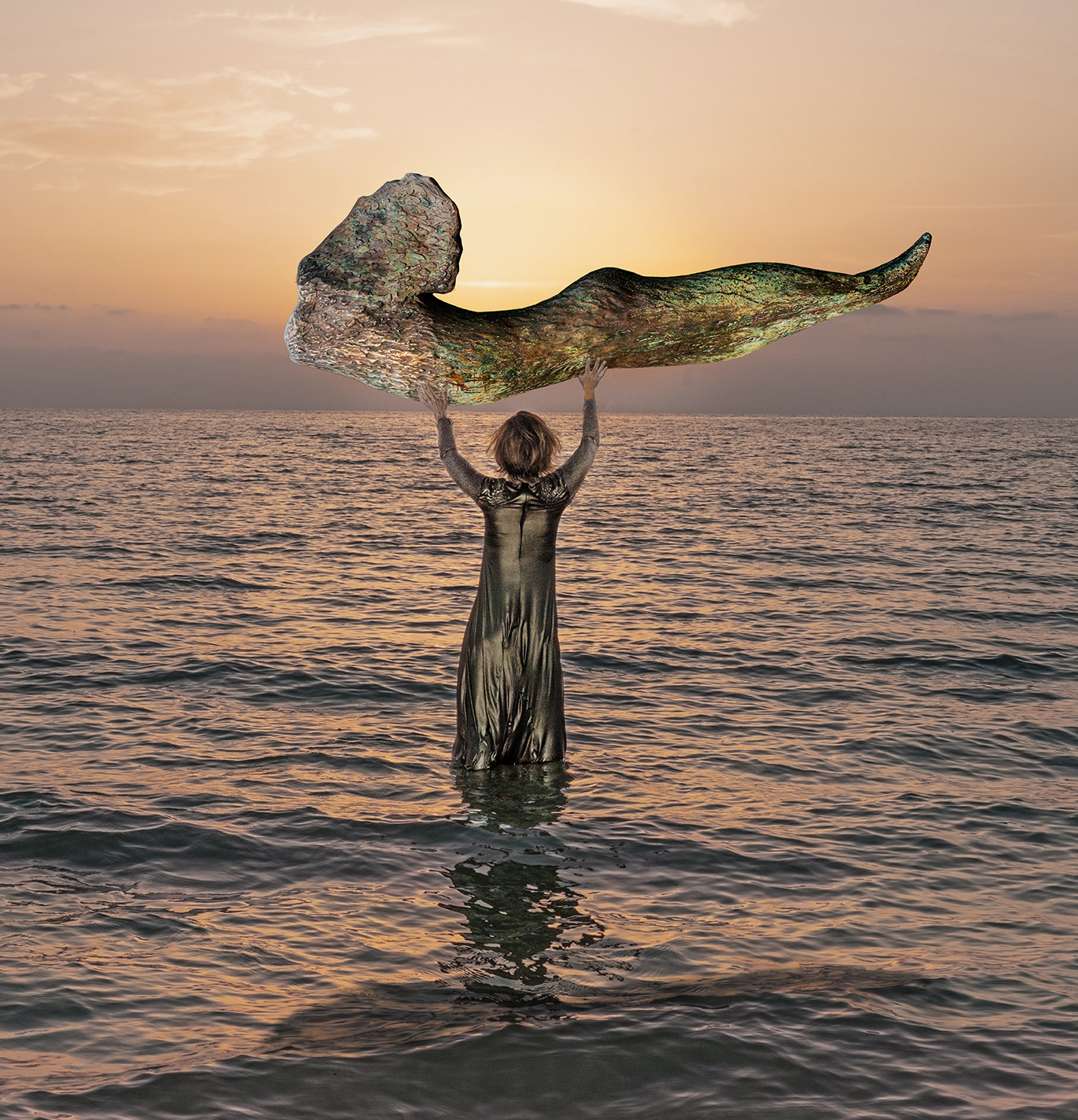 figure standing in ocean holding sculpture above head