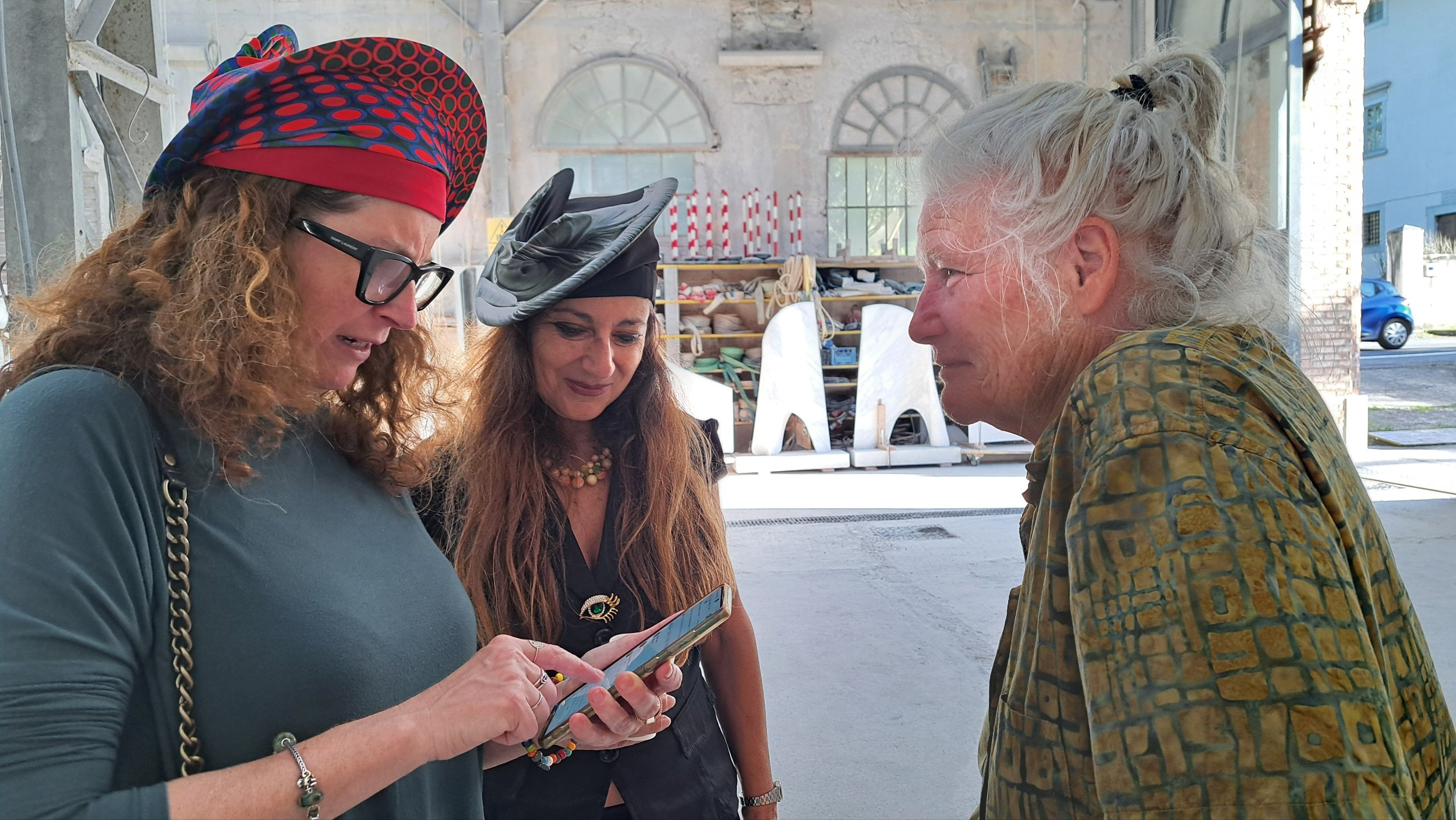 three women in an artist's studio, two women are wearing distinctive hats