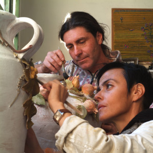 Two artists working on sculpting large pots.