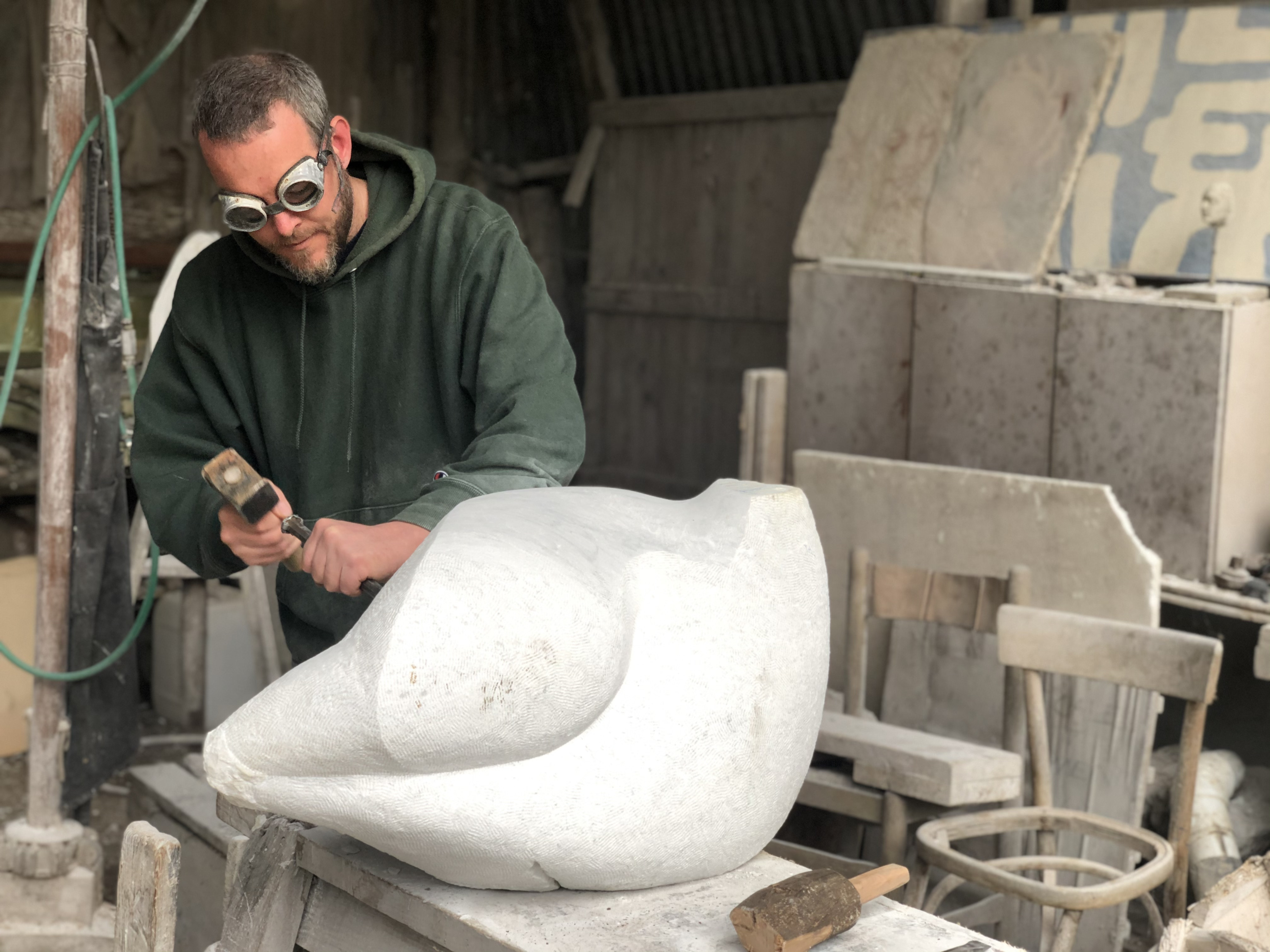 sculptor in goggles using a chisel on stone