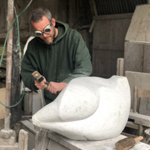sculptor in goggles using a chisel on stone