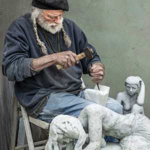 Man carving marble figures on his lap