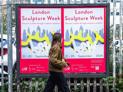 lady walking in front of a London sculpture week poster on iron railed fence