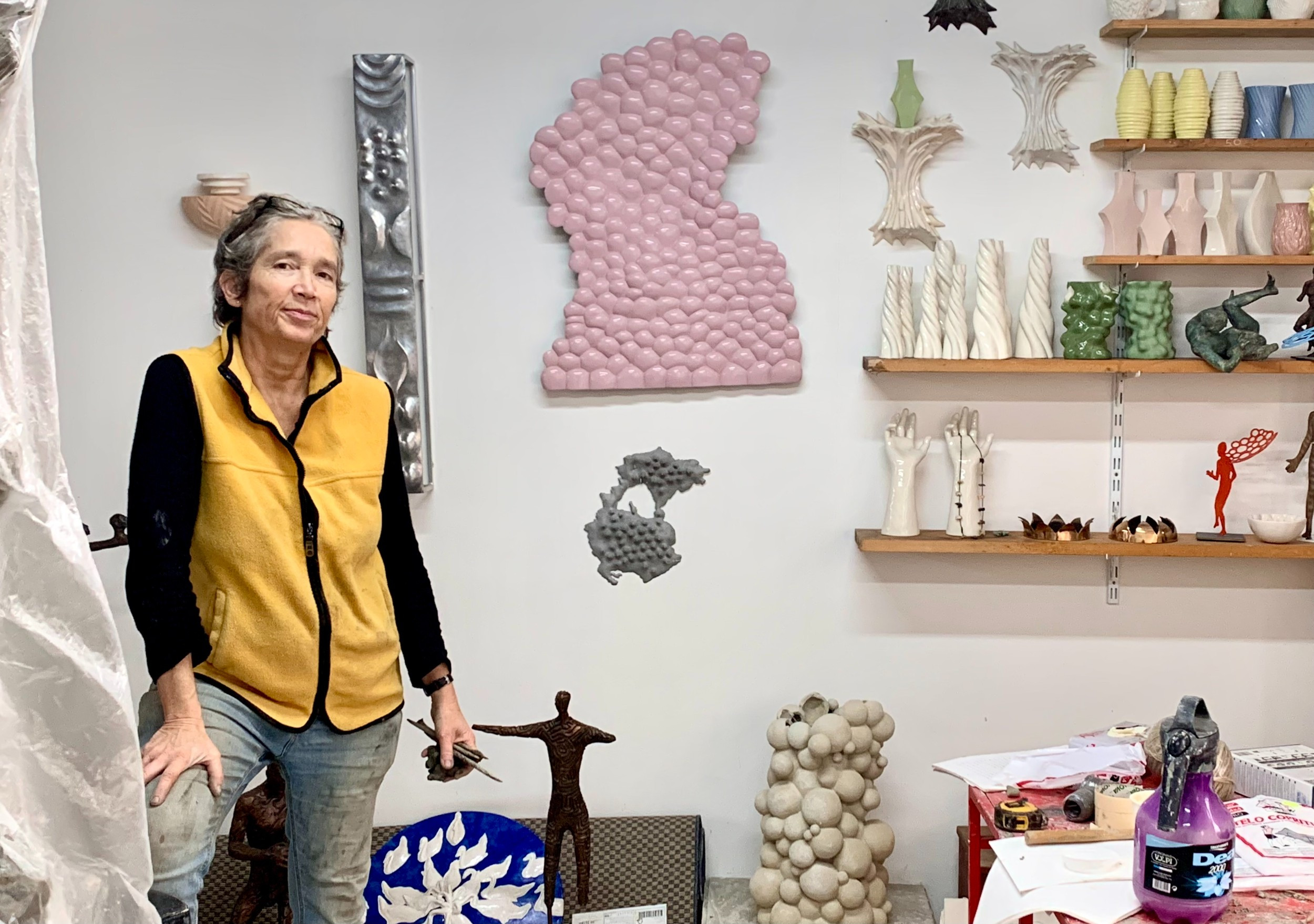 Woman in artist's studio surround by a variety of small, abstract sculptures