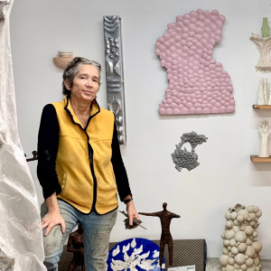 Woman in artist's studio surround by a variety of small, abstract sculptures
