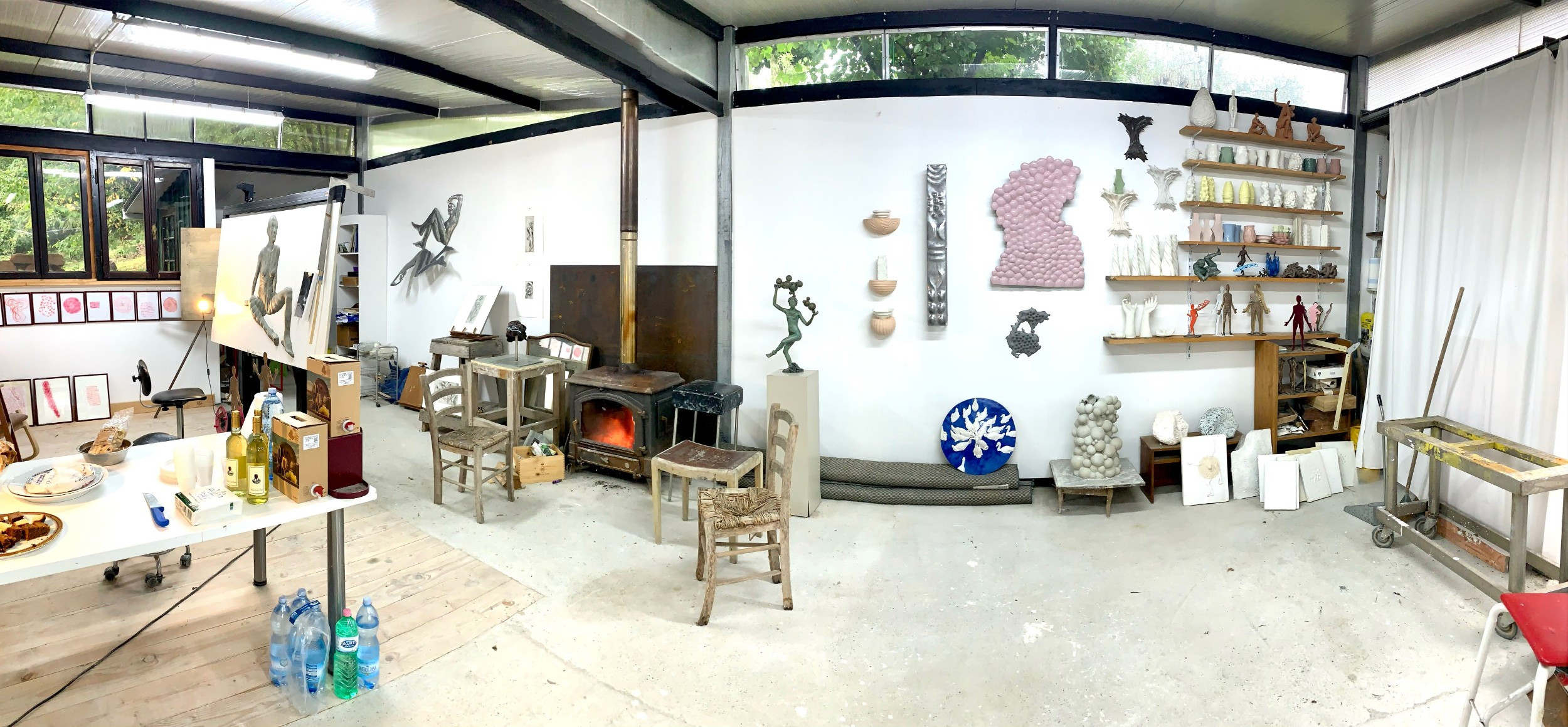 Wide panoramic photo of an artist's studio, sculpture and drawings on the walls, woodstove and a desk