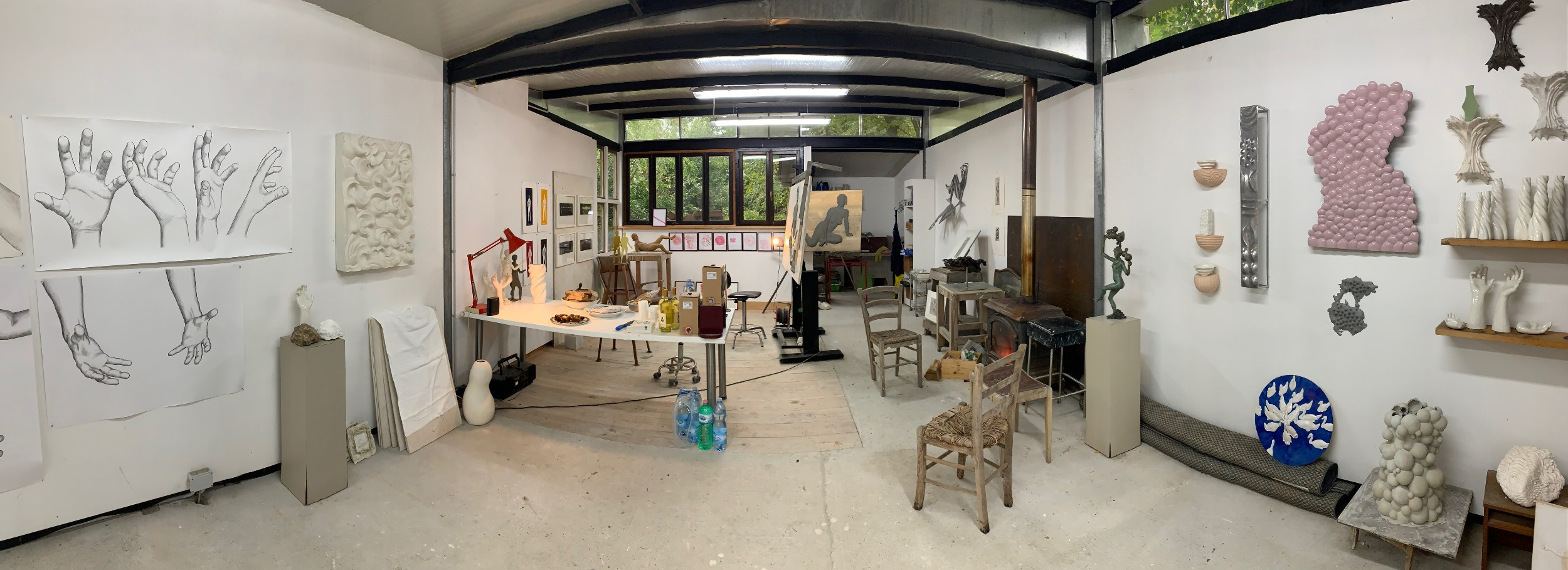 Wide panoramic photo of an artist's studio, sculpture and drawings on the walls
