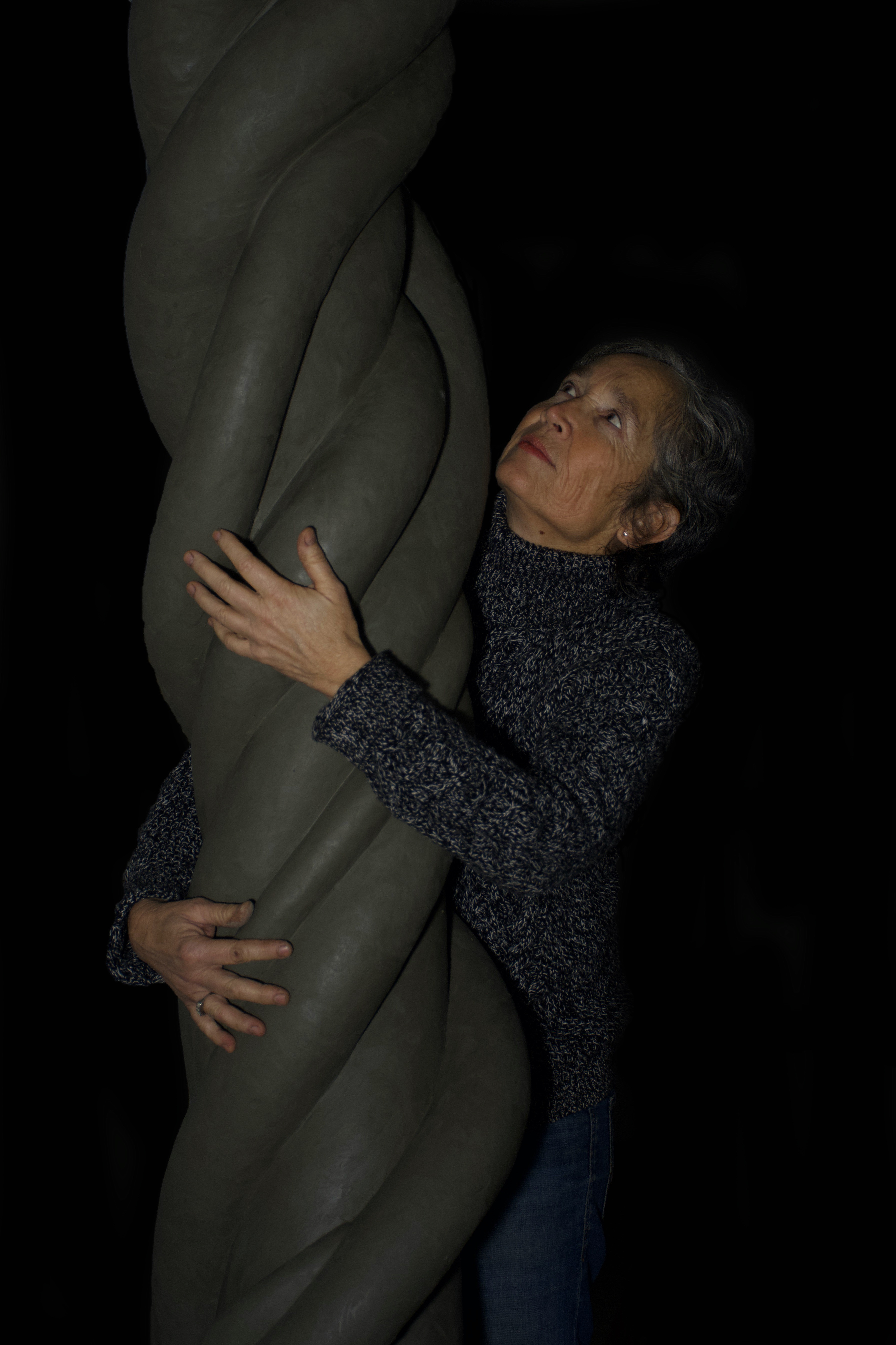 female artist hugging her spiral sculpture on a black backdrop
