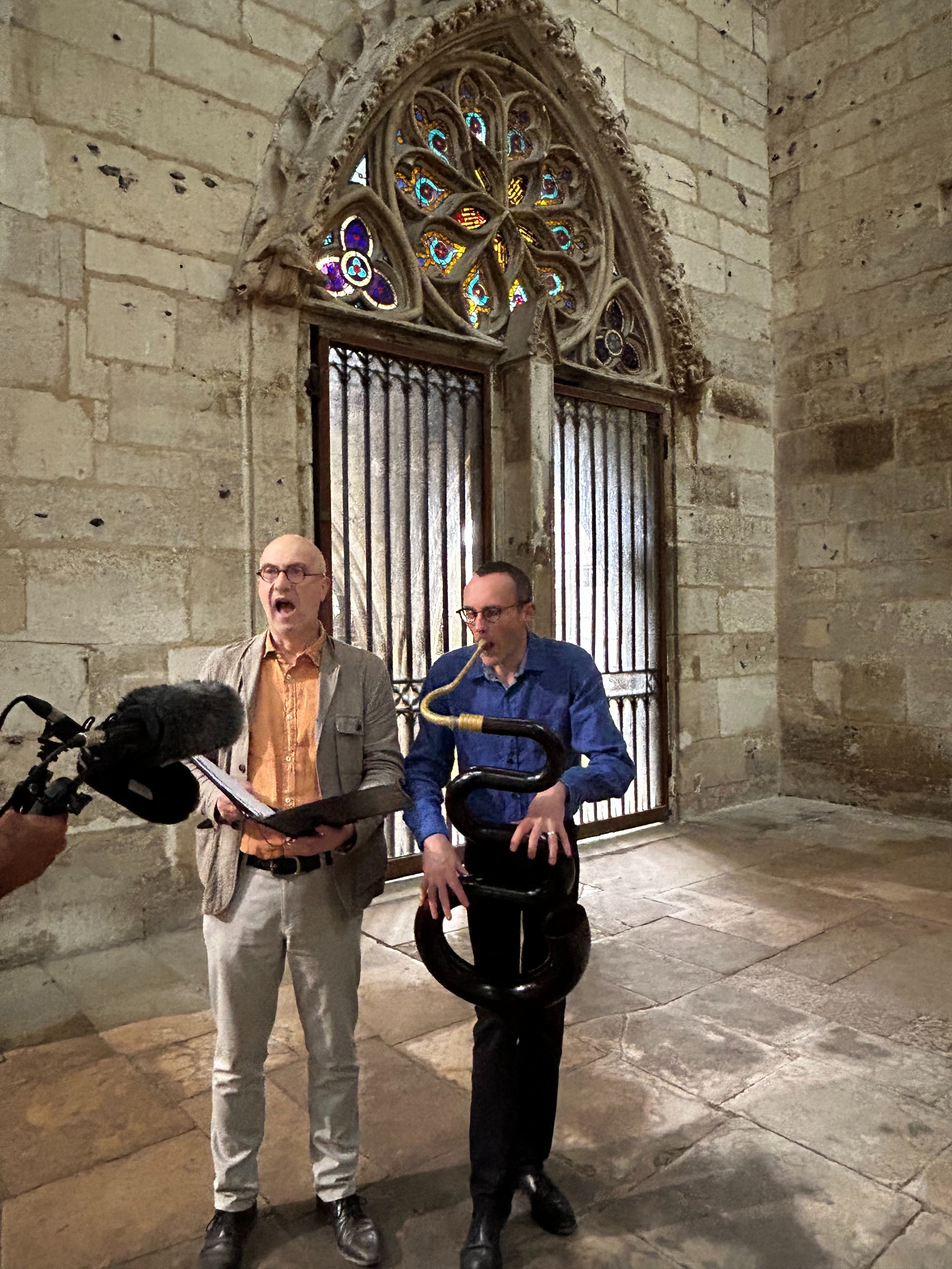 two men in a stone church, one singing, one playing a serpent
