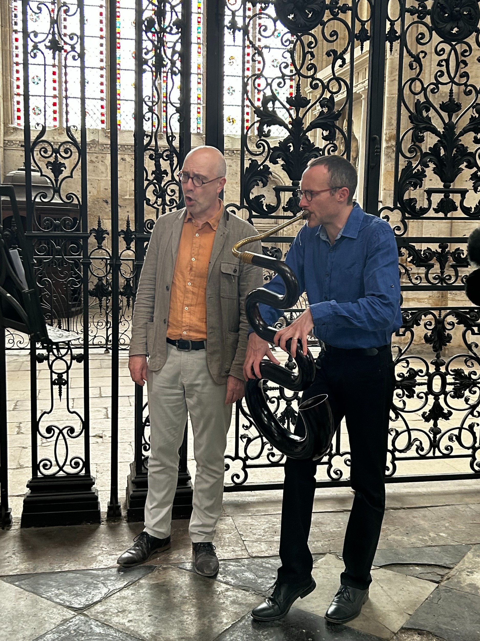 singer and serpent player in front of interior metal gates of a cathedral