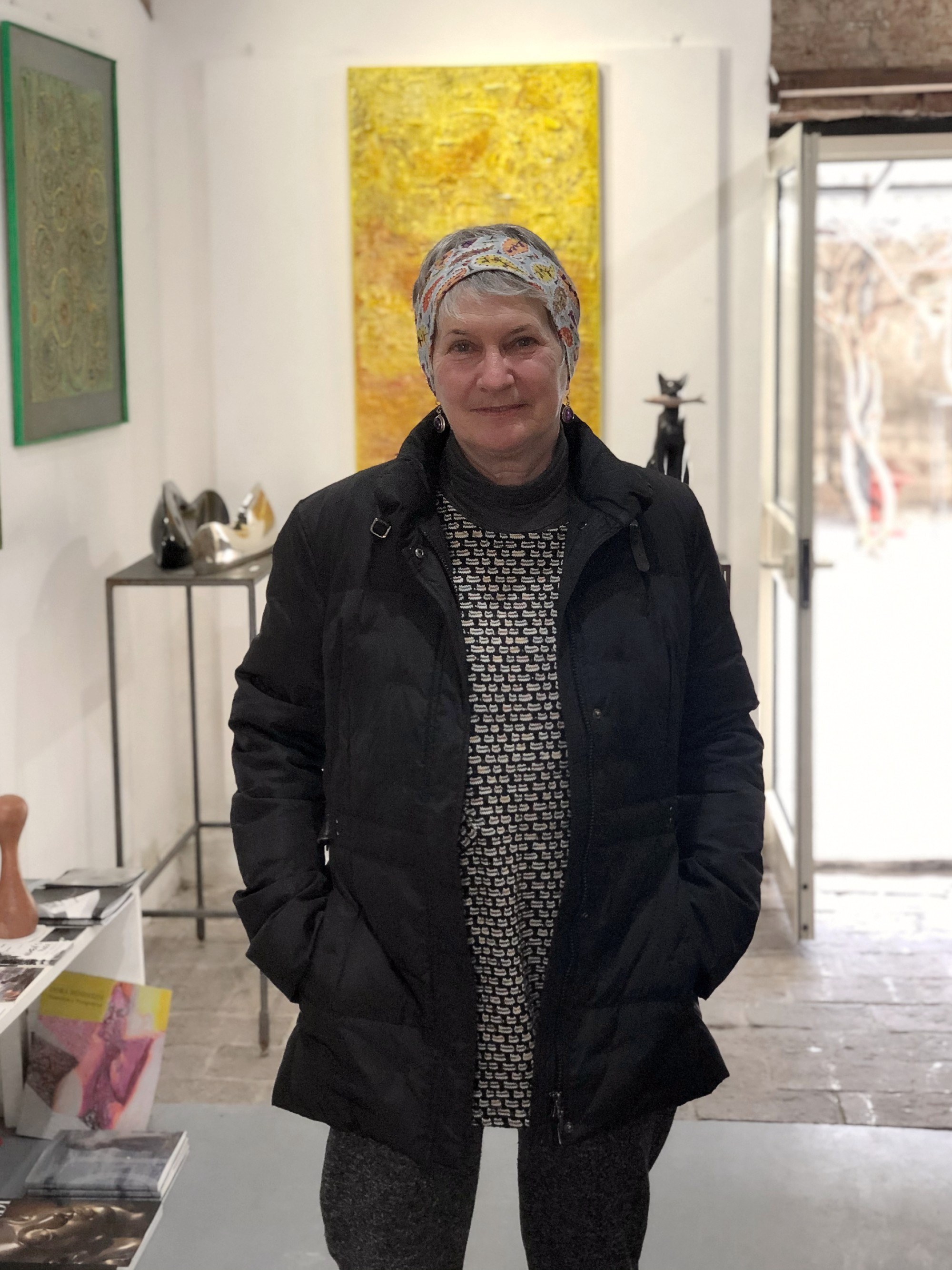 Female artist smiling with hands in pockets in an art studio