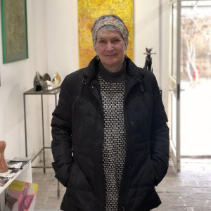 Female artist smiling with hands in pockets in an art studio