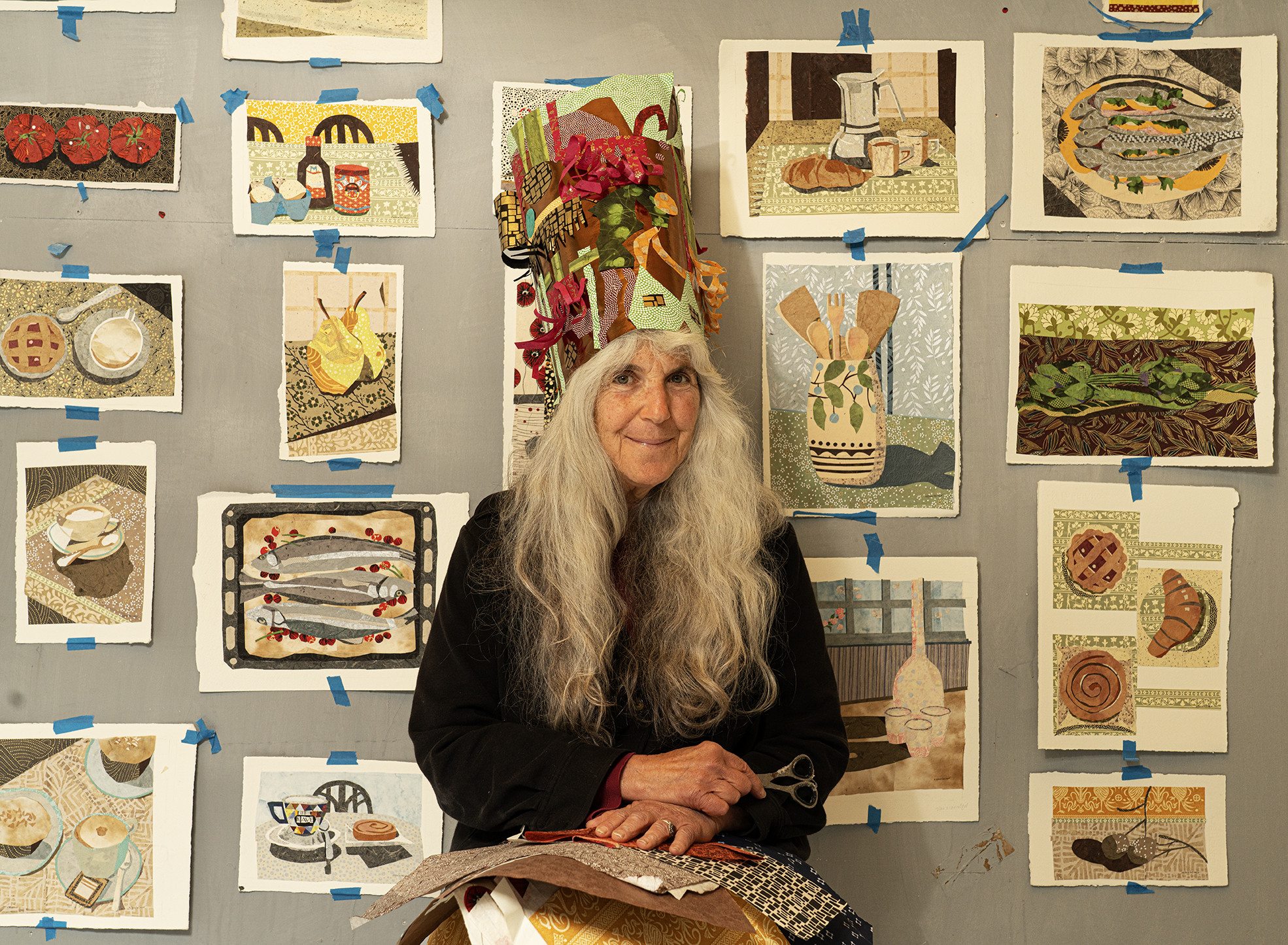 woman wearing a collage hat standing in front of collage artwork taped to a wall