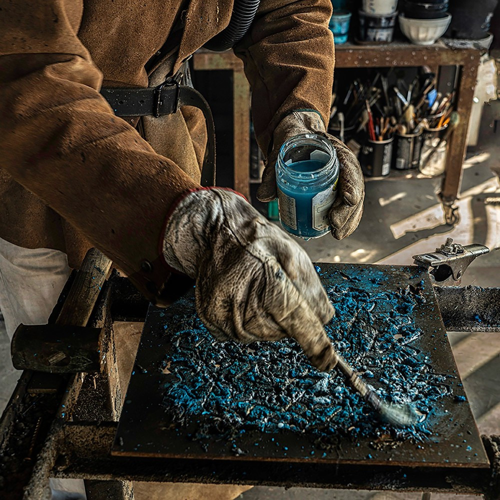 someone spreading a bright blue pigment onto a square of metal
